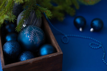 Classic blue Christmas toy balls with sparkles and snowflakes in a wooden box on a background with beads and green fir new year tree branches.