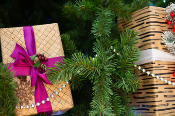 New Year's big boxes with gifts packed in beige paper and decorated with a pink bow, fir branches, purple berries and cones under the Christmas tree.