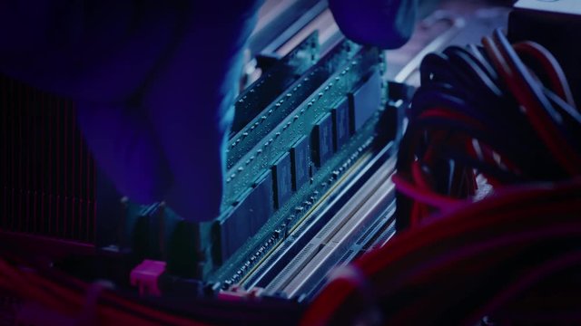 Close-up Moving Macro Shot: Gloved Hand Installs RAM Memory into Computer Motherboard Slot. Technician Upgrades Computer / Server System. Modern High-End PC Shot in Stylish Neon, Pink-Blue Colors. 