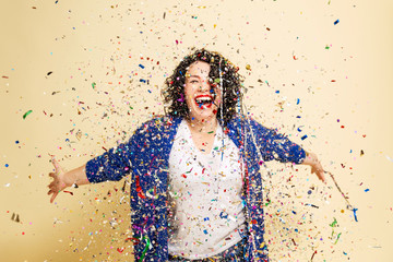 Obraz premium Young beautiful woman with curly hair sprinkled with confetti laughs. Festive mood. Isolated over white background.
