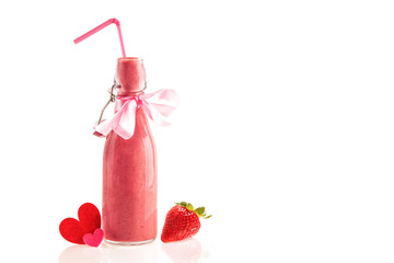 Delicious and nutritious smoothie made from fresh strawberries in a glass bottle with a straw, a pink bow and cloth hearts. Gift to give and share the lovers on Valentine's day. White background.