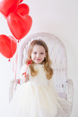Beautiful little girl with red balloons in the shape of a heart at the holiday