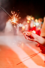 A crowd of young happy people with sparklers in their hands during celebration. Red sparklers at the wedding - bride, groom and guests holding lights in hand. Sparkling lights of bengal fires. Smoke.