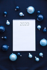 notebook on a spiral for the list of goals for 2020 New year on a dark blue background surrounded by Christmas balls of different shades of blue