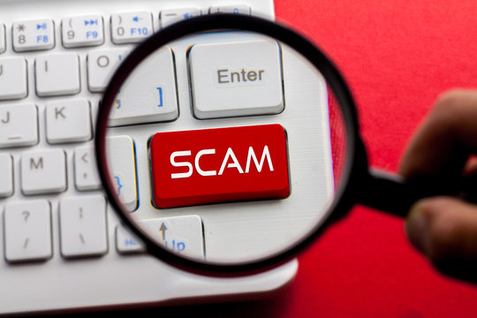 SCAM word written on keyboard view with magnifier glass