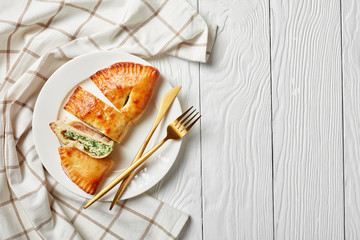 calzones with Spinach and Cheese filling served on a white plate with golden fork and knife on a wooden table, flatlay, copy space