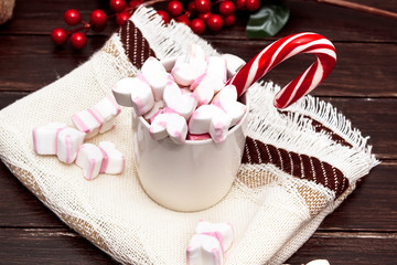 A white cup of hot chocolate with pink marshmallows and christmas candy on dark wooden background. Winter drink. Winter mood.