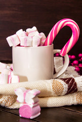 A white cup of hot chocolate with pink marshmallows and christmas candy on dark wooden background. Winter drink. Winter mood.