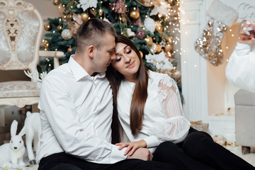 A guy with a girl is celebrating Christmas. A loving couple enjoys each other on New Year's Eve in a cozy home environment. New Year's love story. Happy pair posing near Christmas tree.