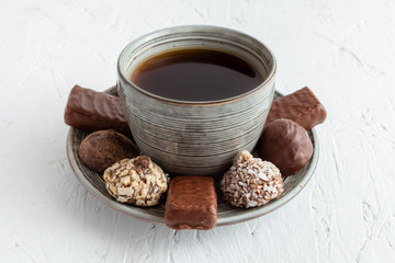 Coffee with many chocolates. Tea cup with plate surrounded by an abundance of chocolate assortment carefully arranged.