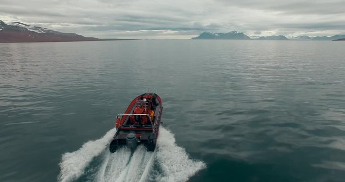 Svalbard. A speedboat with two passengers on the board move fast by the water surface of aArctic Ocean. Splashes of water fly off to the sides. The white wake follows the vessel. Aerial top view.