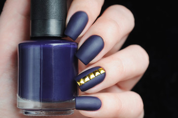 violet manicure with gold metallic rivets on black background
