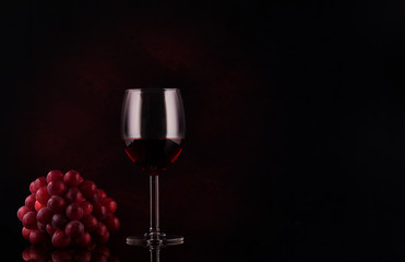 small branch of grape and glass with wine on black background with reflections and copy space. Concept sales, discount price. Photo for banner