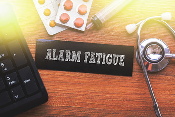 ALARM FATIGUE words written on label tag with medicine,syringe,keyboard and stethoscope with wood background,Medical Concept