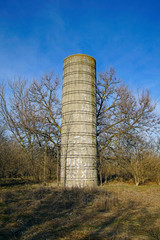 Abandoned concrete grain Silo stands in an overgrown field