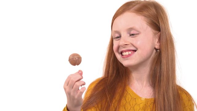 Close-up of foxy haired girl with green eyes eating candy. Little child eating sweet lollipop