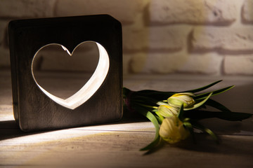 Nice tulip bouquet laying on wooden table near creative night lamp with heart cutout in front of...