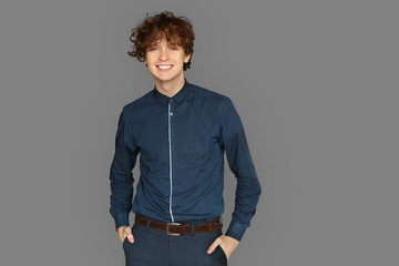 Freestyle. Teenager boy standing isolated on grey hands in pockets smiling cheerful