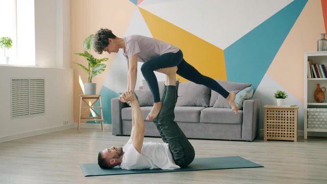 Joyful couple is practising pair yoga together doing support asanas in apartment, man and woman are enjoying activity. Healthy lifestyle and house concept.