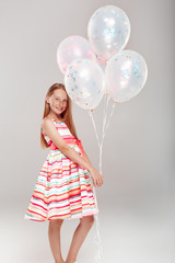 Inclusive Beauty. Girl with freckles in dress standing isolated on grey holding balloons posing smiling joyful