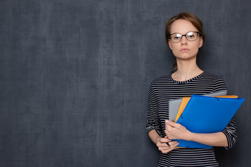 Portrait of serious focused young woman holding folders and pen