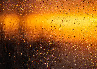 Rain drops on a window during a sunset creating a golden abstract background or wallpaper