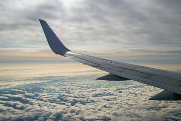 Obraz premium Fluffy carpet of clouds stretching to horizon spreads out under wing of plane against background of morning dawn sky and pink band on the horizon illuminated by rays of sun breaking through from above