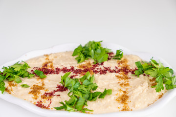 Homemade humus on a white plate with tahini, spicy, olive oil, lemon, parsley and chickpeas. Arabic food, appetizer - Delicious humus. Selective focus.