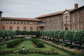 Obraz premium Hospital architecture of the Hotel Dieu in Toulouse France. Photography of an old medieval three-story european building from with a green plant garden in the courtyard.