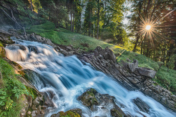 Wild waterfall in forest at sunset