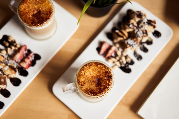 Two cups of Hot latte with baked caramel crust and sweet roll with banana and strawberry on the wooden table in coffe-sho. Coffee concept. Top view photo of two sets