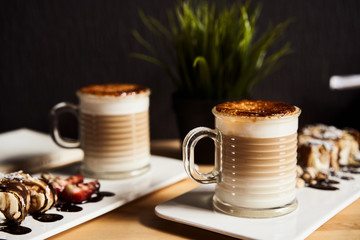 Two cups of Hot latte with baked caramel crust and sweet roll with banana and strawberry on the wooden table in coffe-shop. Coffee concept