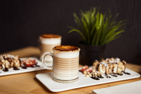 Two cups of Hot latte with baked caramel crust and sweet roll with banana and strawberry on the wooden table in coffe-shop. Coffee concept