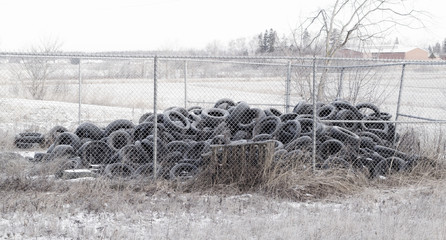 Pile of old tires behind chain-link fence on a cold and frosty day.