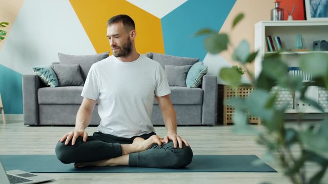Young man doing yoga with video tutorial on laptop