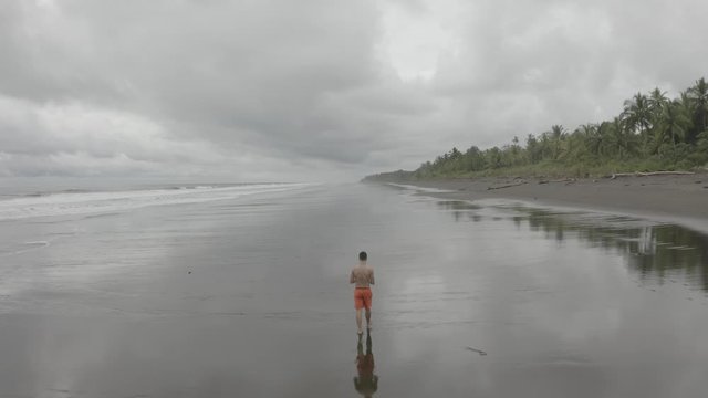Aerial flying over a young guy walking at an empty Beach in Colombia.