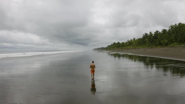 Aerial follows a young man that walks on an empty beach, Colombia.