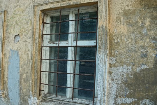 white old wooden window behind a brown rusty grate on the concrete wall of the building