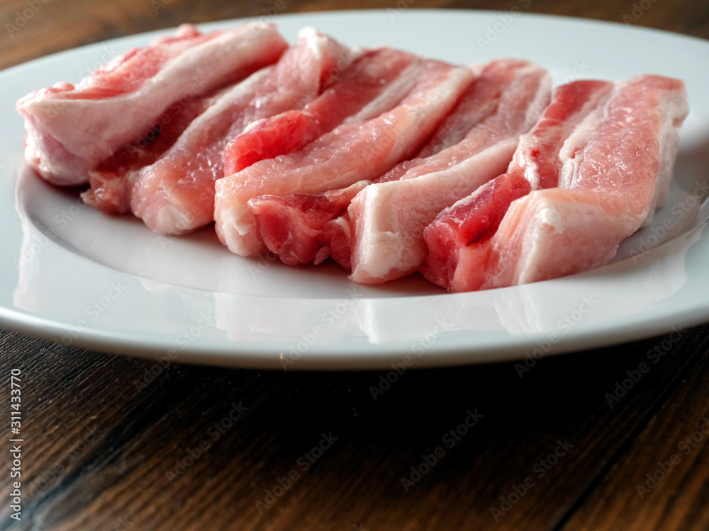 Wall mural fresh uncooked pork belly slices on a white plate. wooden table surface.