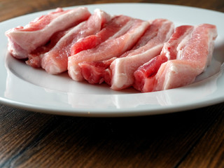 Fresh uncooked pork belly slices on a white plate. Wooden table surface.