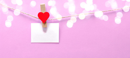 Happy Valentine's Day background banner - White paper note hang on wooden clothes pegs with wooden hearts on a string isolated on pink texture and bokeh lights, with space for text