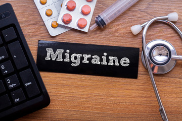 Migraine words written on label tag with medicine,syringe,keyboard and stethoscope with wood...