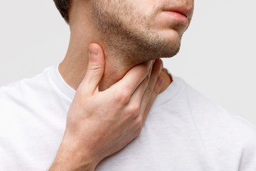 Close up of sick man suffering from throat problems, grey background, isolated. Thyroid gland,...