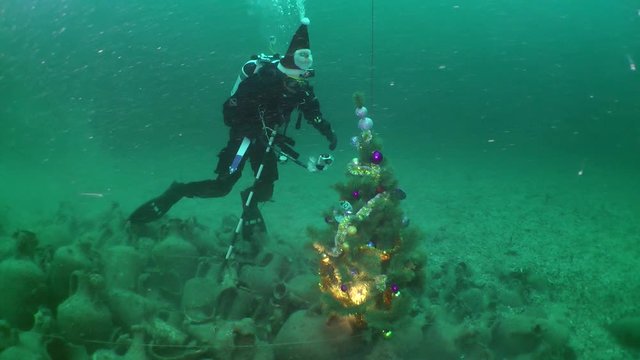 Archaeological divers celebrate the New Year under water: a diver in a Santa hat is filming a Christmas tree on a pile of ancient amphoras.