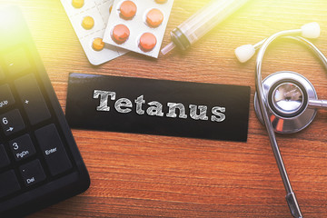 TETANUS words written on label tag with medicine,syringe,keyboard and stethoscope with wood background,Medical Concept