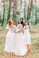 Obraz na płótnie Canvas Bride and bridesmaids in white dresses posing on the forest background outdoors. Bride holding her wedding bouquet. Rustic wedding in the forest