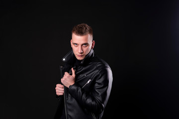 Portrait of handsome man in black, man pulling his leather jacket's collar on black studio background.