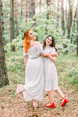 Funny two beautiful girls bridesmaids dance in the forest. Two bridesmaids in white dresses and wreaths on the heads smiling and having fun together