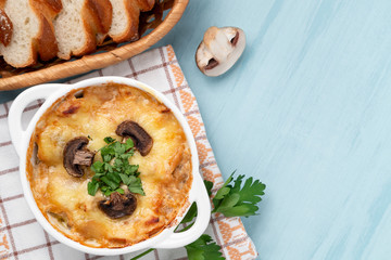 Casserole with chicken, mushrooms and cheese known in Russia as julienne in white bowl with herbs on a blue table, top view, flat lay, copy space