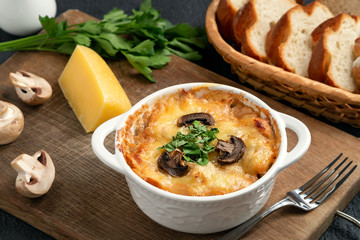 Casserole with chicken, mushrooms and cheese, known in Russia as julienne in white bowl with herbs on a wooden board, close up
